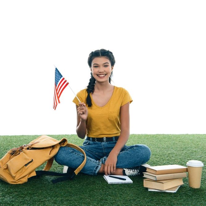 jovene studiante sentada en cesped artificial sosteniendo bandera de estados unidos de america